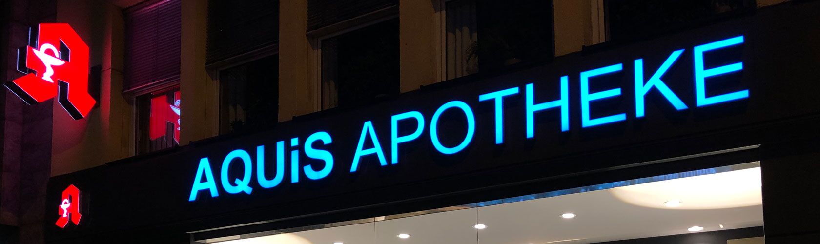 Das leuchtende Schild der Aquis Apotheke zeigt ihren Notdienst an einem Abend in der Stadt an.