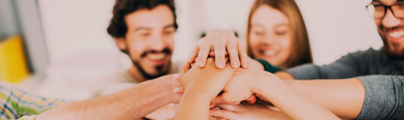 Ein Team von Menschen legt motiviert die Hände übereinander, um den Zusammenhalt und den Start einer neuen Karriere zu symbolisieren.